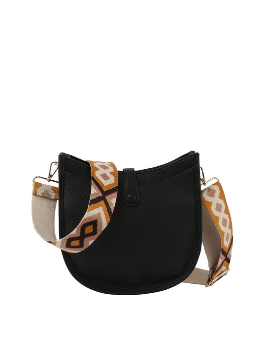 The Guitar Strap Structured Hobo Handbag is a black, crescent-shaped faux leather bag with a wide, adjustable strap in a brown, beige, and white geometric pattern. Tablet compatible, it closes with a single front button.