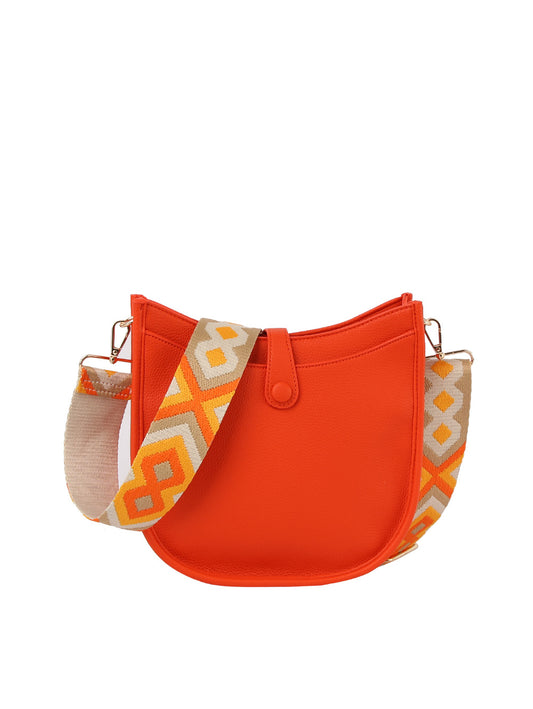 The Guitar Strap Structured Hobo Handbag is a bright orange faux leather bag with a rounded shape, snap closure, and a wide strap featuring a yellow, orange, and cream geometric pattern. Tablet compatible. Displayed on a plain white background.