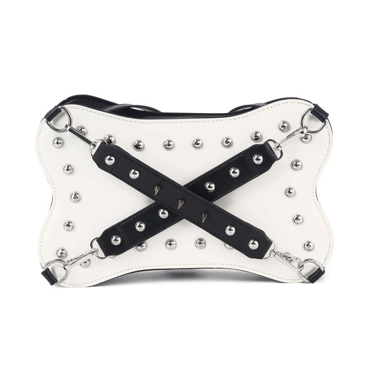 The Studded Belted Shoulder Bag features white faux leather with black X-shaped straps, silver studs, and metal rings for a bold, edgy look. Stylish and tablet compatible.