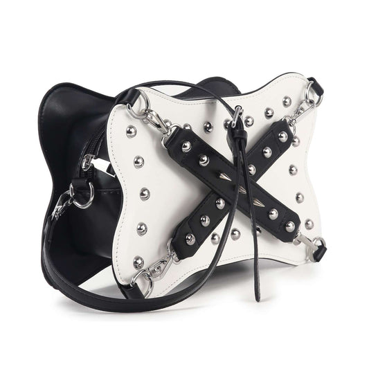 The Studded Belted Shoulder Bag features black and white faux leather, silver hardware, metal studs, crisscrossed black straps on the front, a curved structured shape, zip pocket detail, and a long shoulder strap.