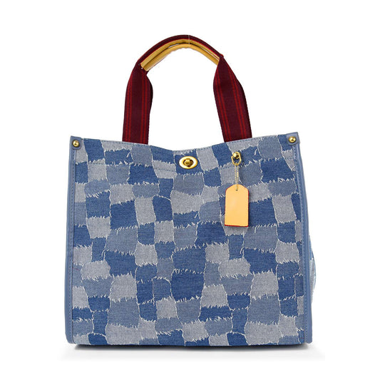 The Denim Print Contrast Tote Handbag features a blue and light blue check print, red handles, gold hardware, a rectangular tan tag at the top, and an adjustable strap for versatile carrying.