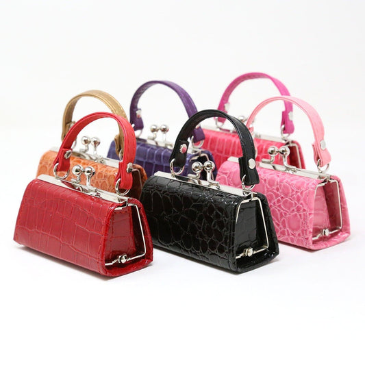 The Patent Alligator Embossed Lipstick Case Assorted Set displays six small faux leather cases—orange, tan, purple, black, pink, and light pink—each with a short handle and metal clasp for storing lipsticks or cosmetics.
