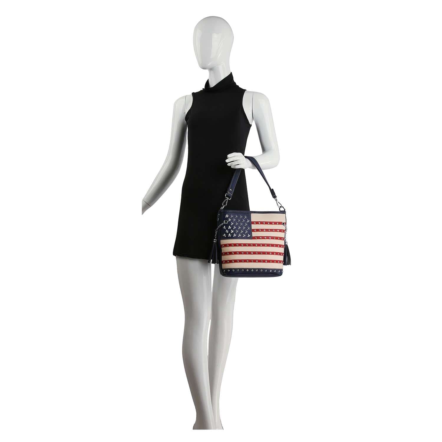 A mannequin in a sleeveless black dress holds the American Flag Hobo Crossbody, a faux leather sling bag with red and white stripes and white stars on a blue background.