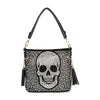 The Sparkling Jolly Skull Hobo Crossbody is a black faux leather bag with a large white rhinestone skull, stud accents, gold hardware, and black tassels on each handle side.