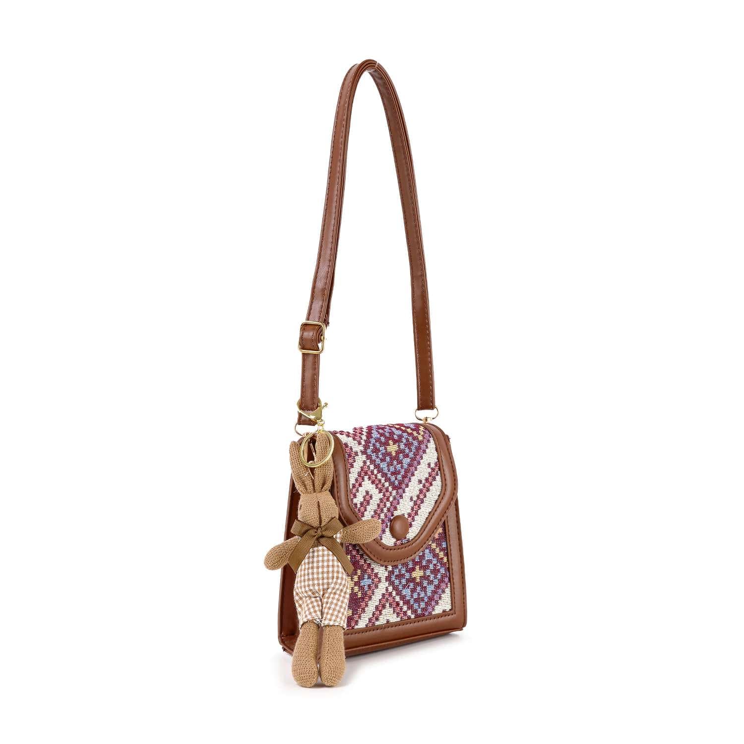 The Decorative Accent Shoulder Bag is a brown lightweight crossbody with a purple and pink patterned flap and includes a small brown teddy bear keychain on its adjustable strap.