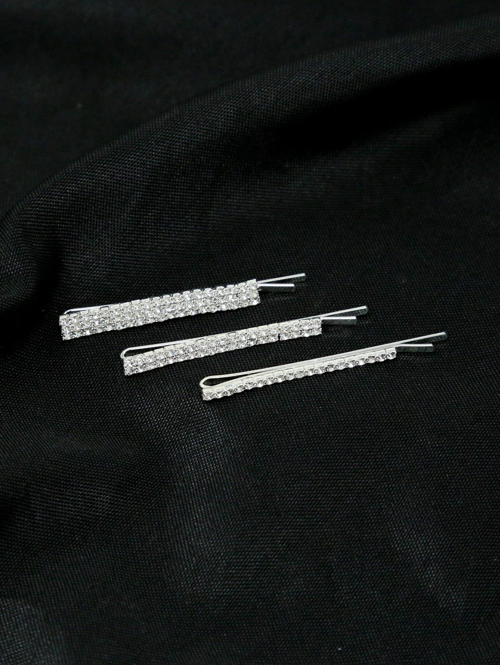 The Set of 3 Rhinestone Hair Clips features sparkling stones on a black fabric background, ideal for layering or adding shine to your favorite hair accessories.