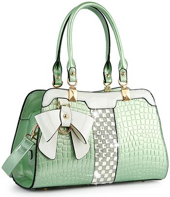 The Brilliant Bow Sparkling Hand Tote is a light green faux leather croc bag with white accents, gold hardware, a white and gold decorative bow, and a silver-and-white checkerboard central strip.