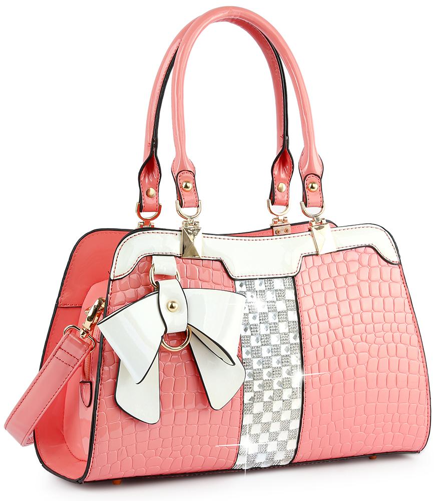 The Brilliant Bow Sparkling Hand Tote is a stylish pink faux leather handbag featuring embossed croc texture, dual handles, a large white bow, gold hardware, and a central white and gray checkered accent panel.