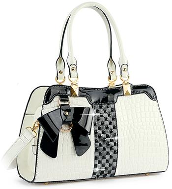 The Brilliant Bow Sparkling Hand Tote is a chic white faux leather bag with crocodile texture, gold hardware, black accents, double handles, a large black bow, detachable strap, and a vertical checkered black pattern.