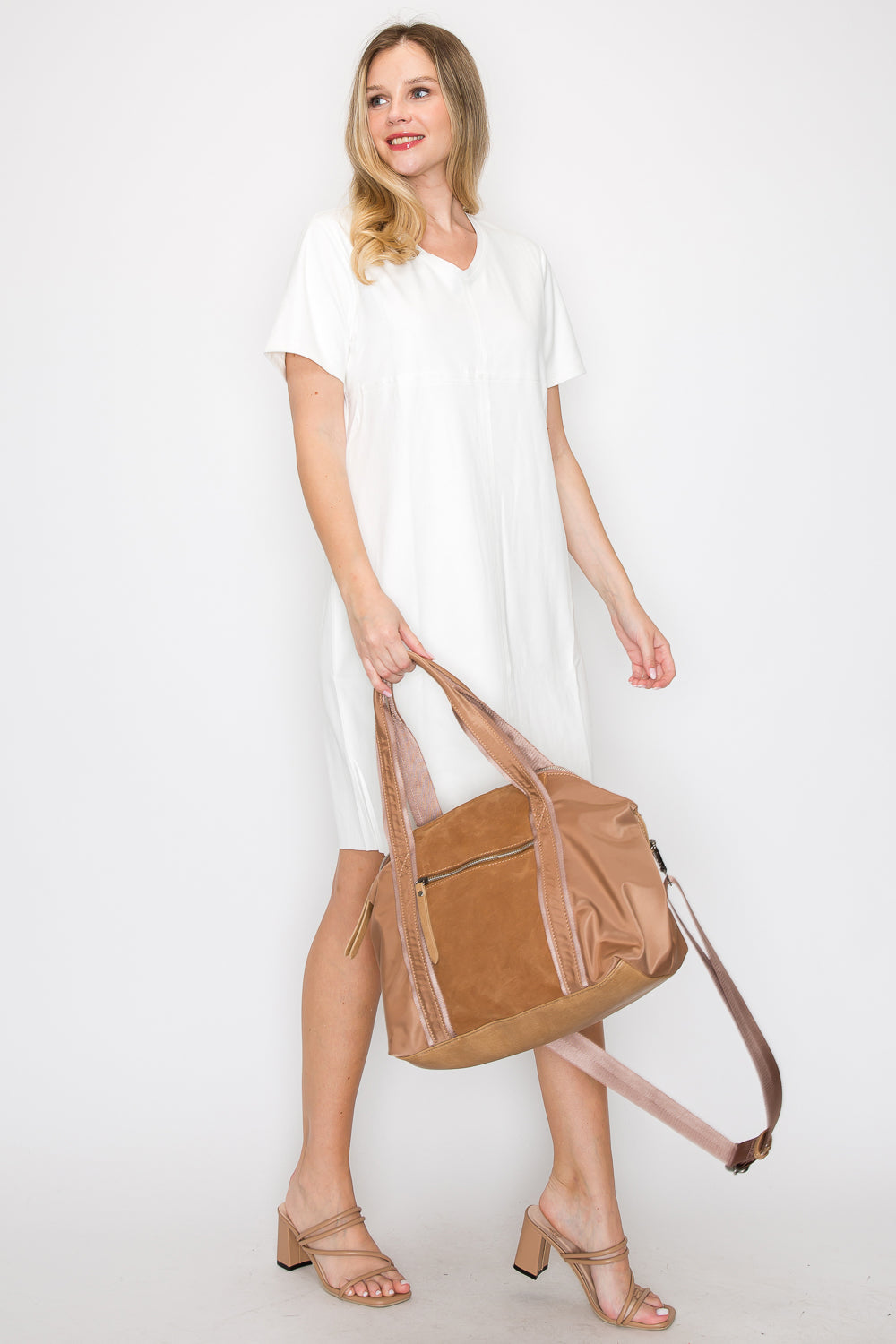 A woman stands against a white background, slightly smiling to the side, wearing a loose white dress and beige heeled sandals while holding the Genuine Leather Classic Fashion Carry All—a large tan tote with a long strap.