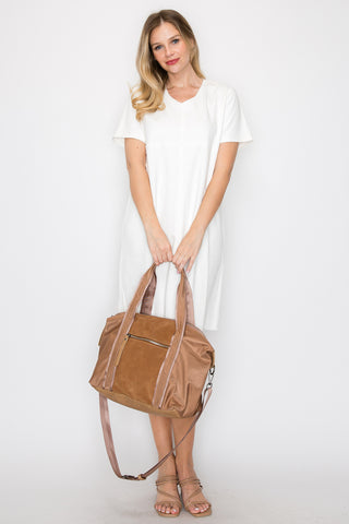 A blonde woman in a white short-sleeve dress stands against a white background, holding the Genuine Leather Classic Fashion Carry All with beige handles and a shoulder strap. She wears strappy sandals and smiles slightly.