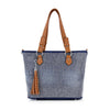 The Rhinestone Denim Fashion Tote is a blue and white patterned tote handbag with brown leather handles, accents, and a matching decorative tassel hanging from one handle.