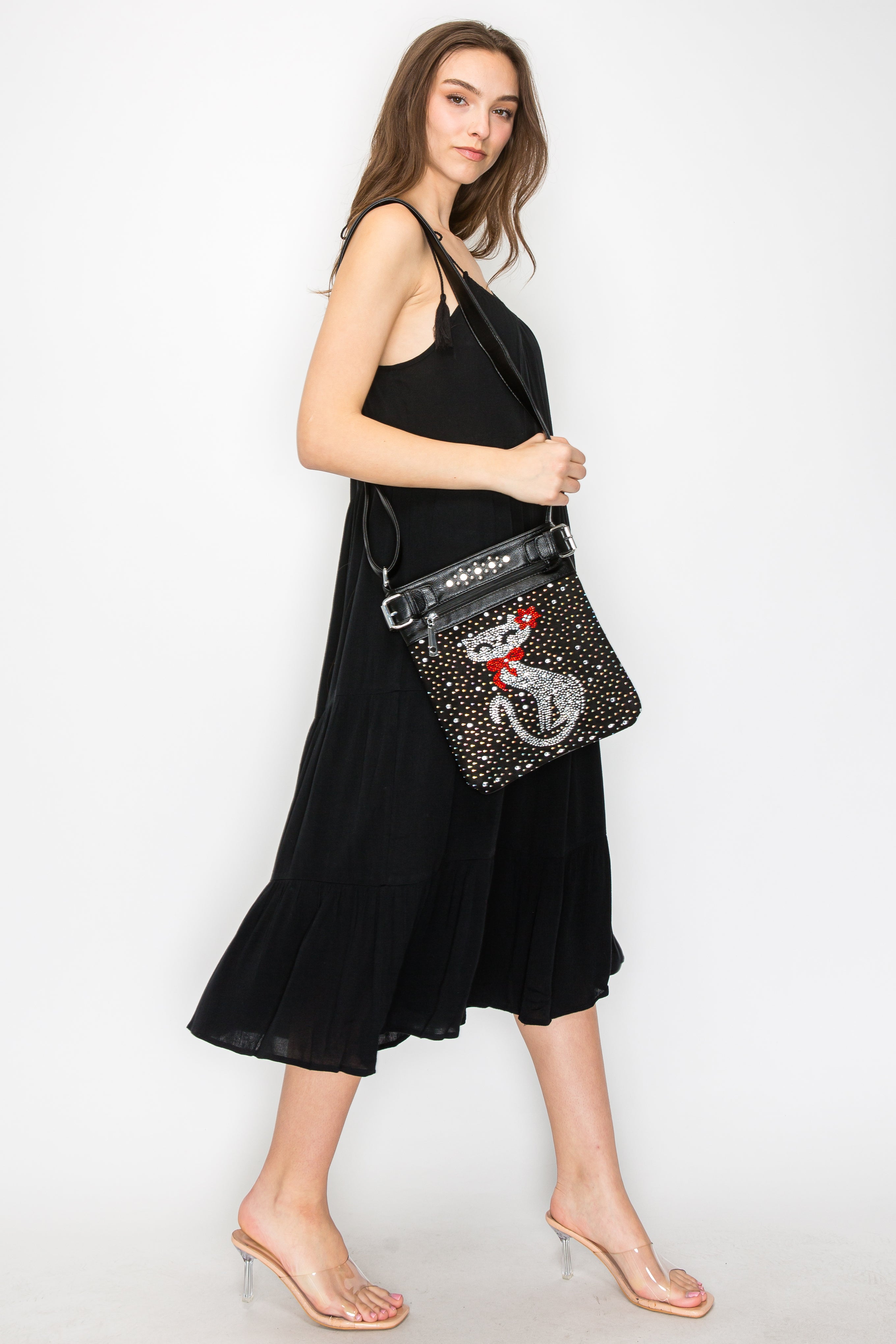 A woman in a sleeveless black dress and clear heels stands sideways, holding the Cat Design Rhinestone Crossbody Sling against a plain white background.