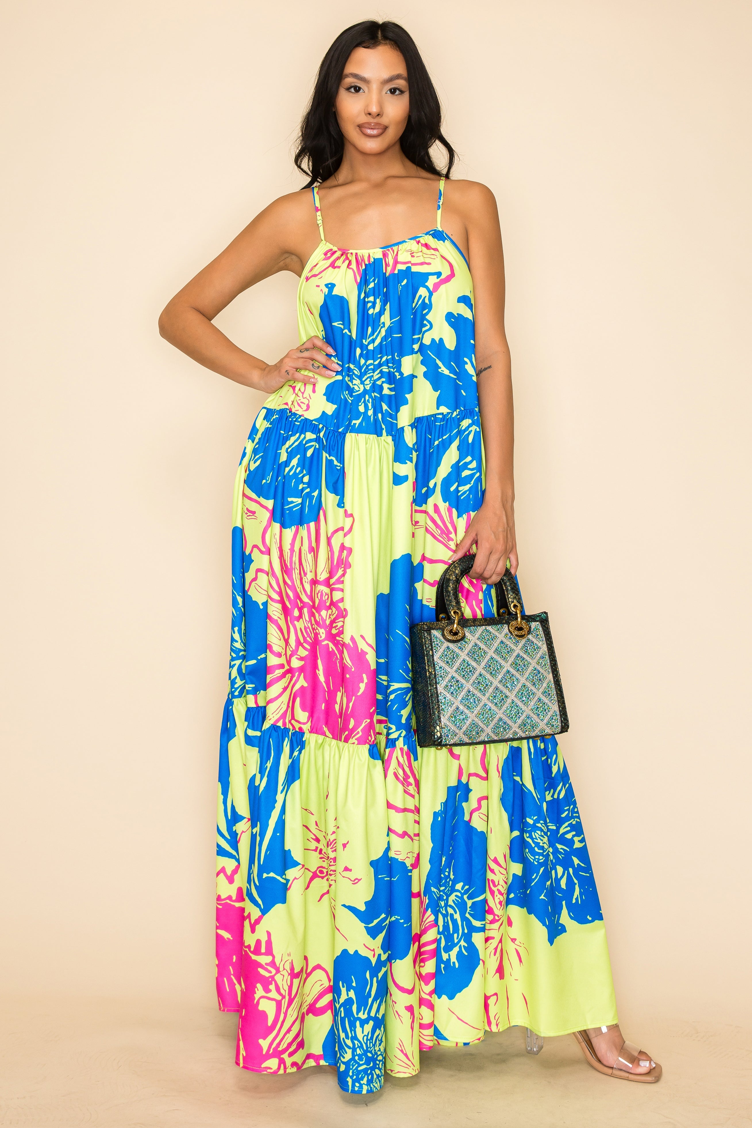 A woman smiles in a long, flowy floral dress and clear heeled sandals, holding the Colored Stone Grid Pattern Tote Handbag, as she poses against a plain beige backdrop.