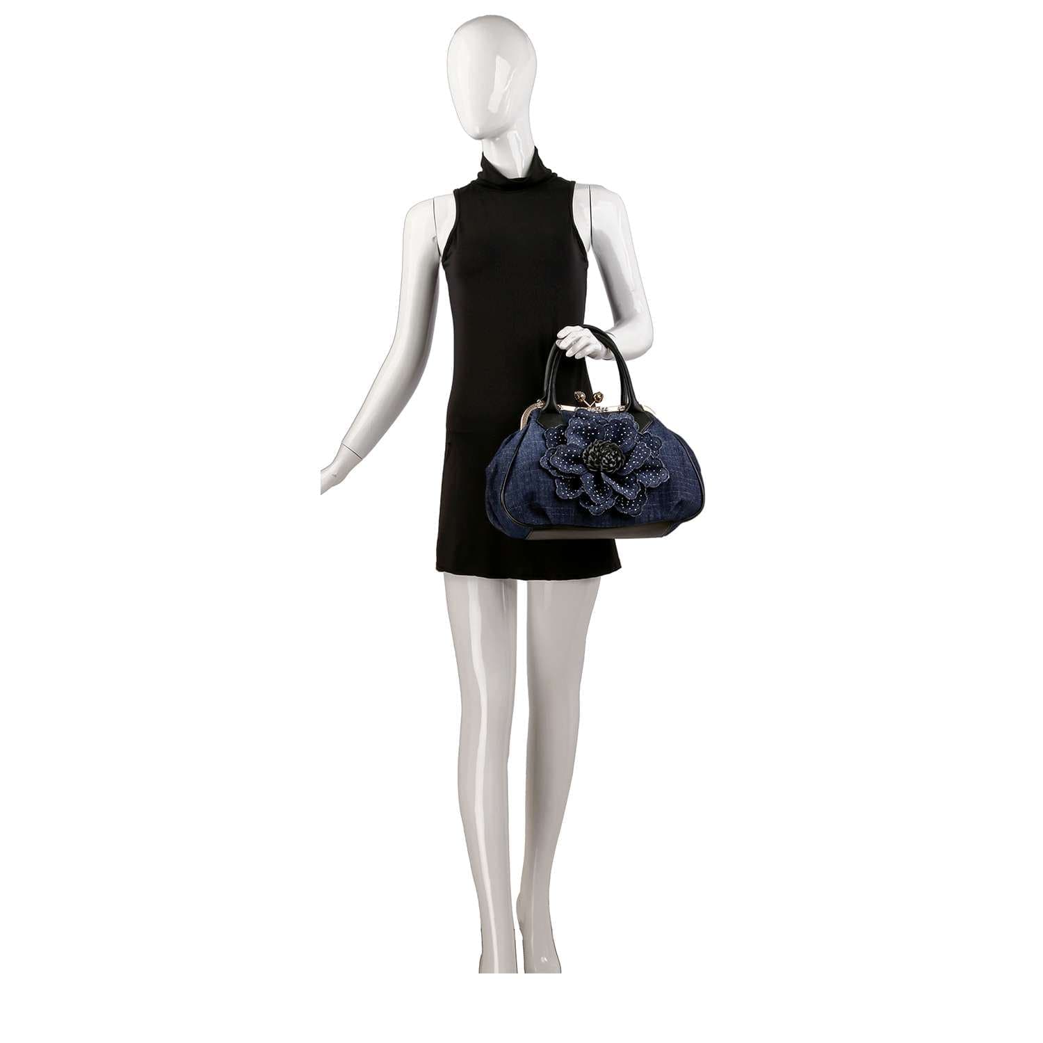 A mannequin in a sleeveless black dress holds the Raised Flower Metal Frame Hand Tote, a navy blue purse with a bold textured floral design. The background is plain white.