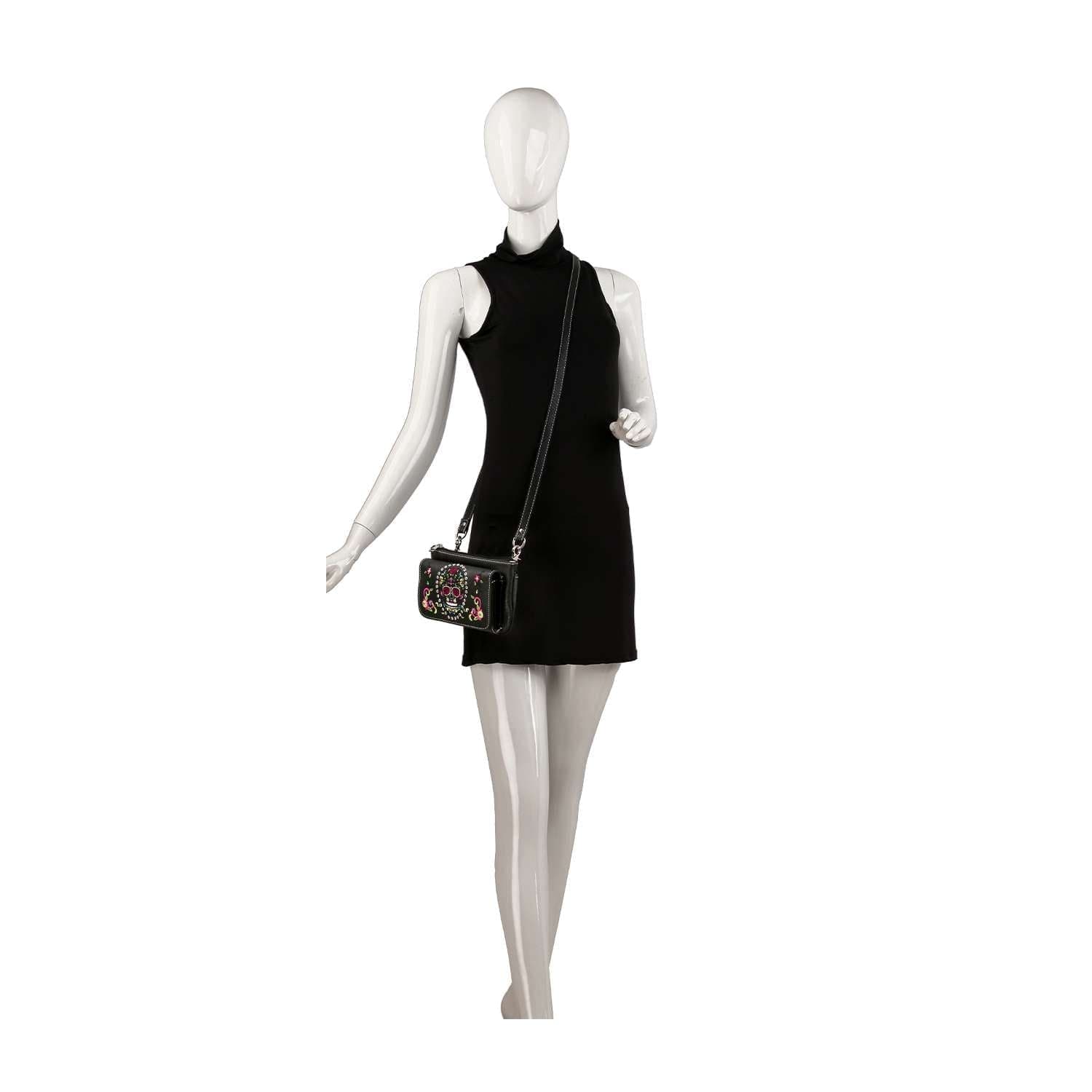 A mannequin in a sleeveless black mini dress carries the Colorful Sugar Skull Petite Crossbody Sling, featuring a vibrant, ornate design and an adjustable strap. The scene is set against a plain white background.