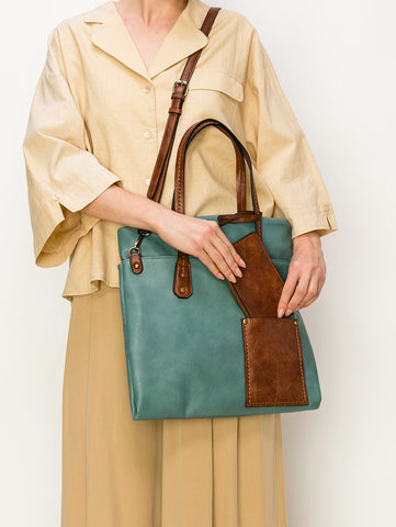 A person stands against a plain white background holding the Two Toned Tall Tote Handbag, a teal faux leather bag with brown handles, trim, an attached pouch, and detachable strap, styled with a beige blouse and skirt.