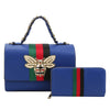 The Bee Pendant Patent Satchel Handbag Set includes a blue faux leather bag with a chain handle and matching wallet, both featuring red and green stripes. The handbag has a front flap adorned with a gold bee pendant, pearl accents, and gold hardware.