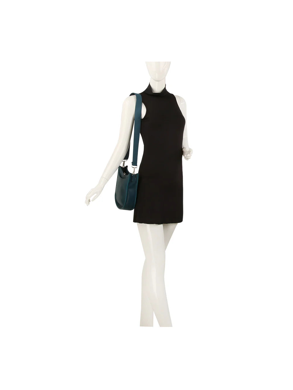 A mannequin in a sleeveless black mini dress carries the Saddle Bag Inspired Curved Crossbody, a dark teal faux leather bag with an adjustable strap, posed with one arm slightly bent and the other relaxed by its side.