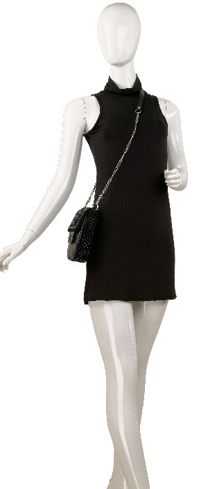 A white mannequin poses with one arm raised, wearing a sleeveless black mini dress and the Decorative Top Flap Cell Phone Crossbody—a small black bag featuring a chain strap and silver-toned hardware.