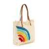 The Canvas Rainbow Design Tote is a cream canvas bag with brown faux leather handles, a textured rainbow pattern, and fringe along the top—stylish and tablet compatible.