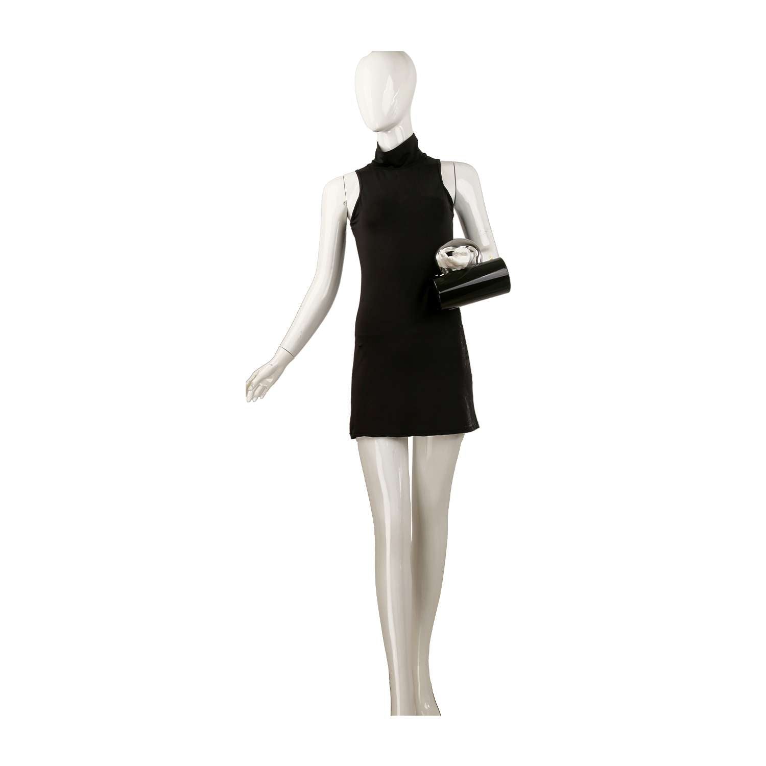 A mannequin in a sleeveless black mini dress holds the Patent Petite Evening Bag, featuring a shiny finish and Art Deco handle, posed against a plain white background.