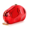 The Modern Patent Petite Shoulder Bag is a shiny red faux patent leather clutch with rounded edges, a gold top clasp closure, and a detachable chain strap placed beside it.