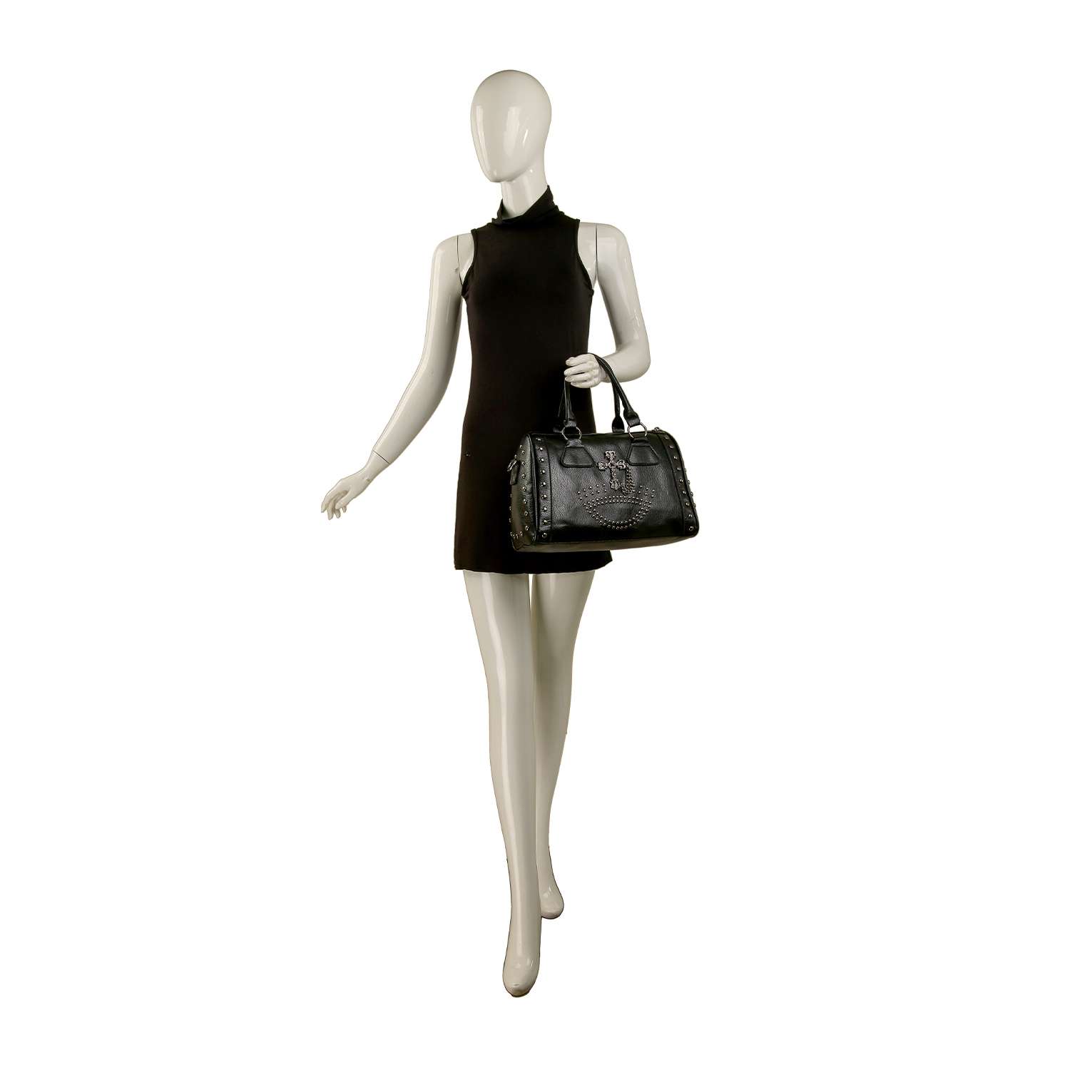 A mannequin in a sleeveless black mini dress holds the Cross And Stud Accented Petite Satchel Handbag by its double handles, standing against a plain white background.