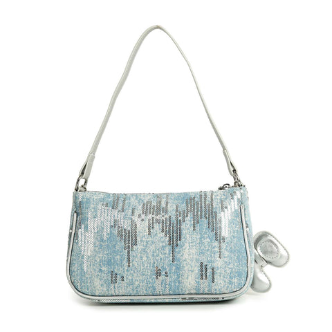 The Denim And Sequin Decorative Hobo is a light blue single-strap shoulder bag with white faux leather trim, silver sequins, a small silver bow charm, and rounded rectangular edges for a chic look.