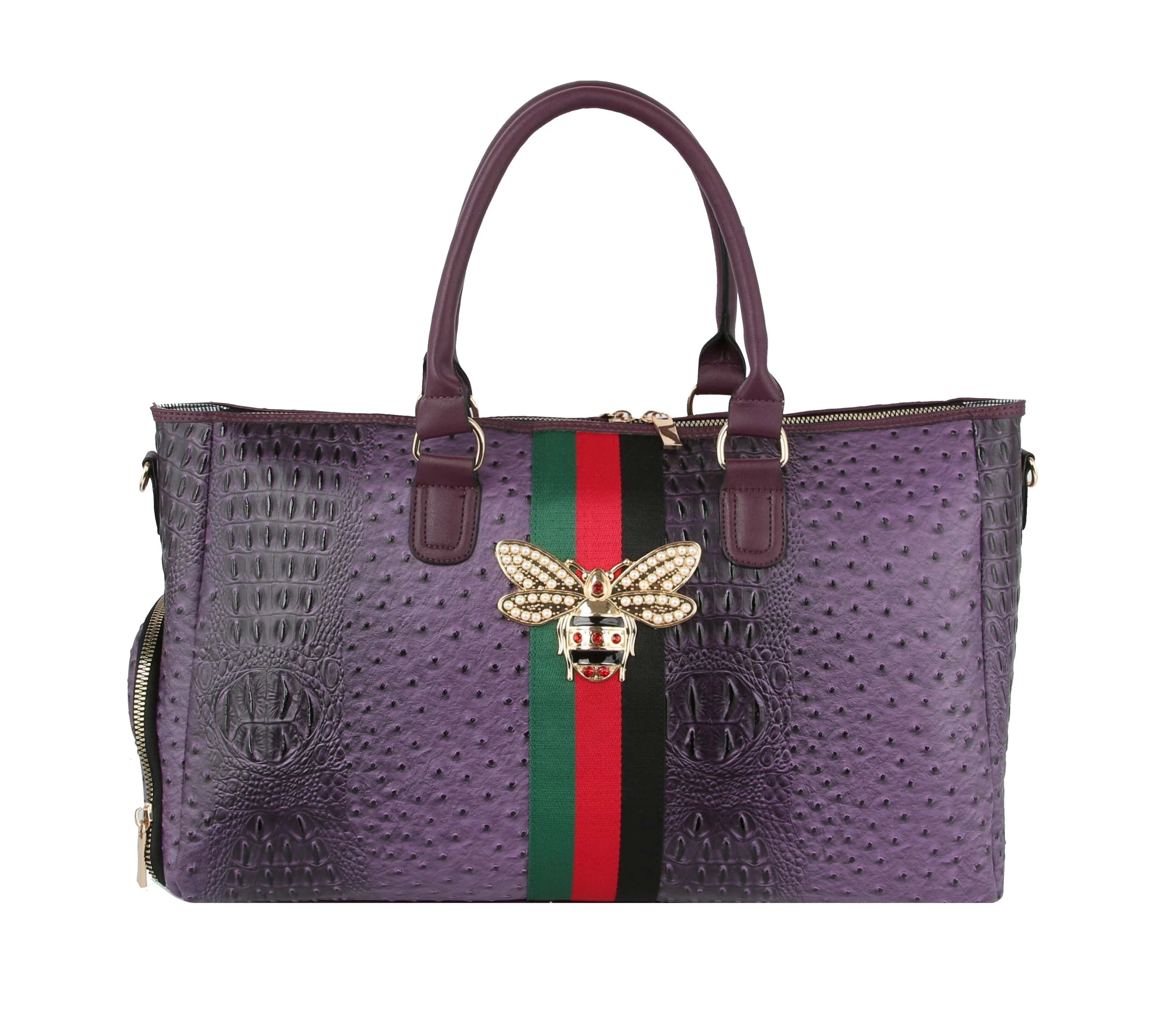 The Croc Embossed Rhinestone Bee Weekender is a purple faux leather handbag with two handles, a green-red central stripe, jeweled bee brooch, gold-tone hardware, side zipper, and detachable strap for versatile styling.