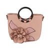 The Raised Flower Tote Handbag in blush pink faux leather has black circular handles, a large 3D flower with leaf applique on the front, gold-toned hardware, and a detachable strap for versatile carrying.