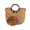 The Raised Flower Tote Handbag features tan faux leather, black circular handles, a prominent 3D brown flower, stitched leaf accents on the front, and comes with a detachable strap for versatile styling.