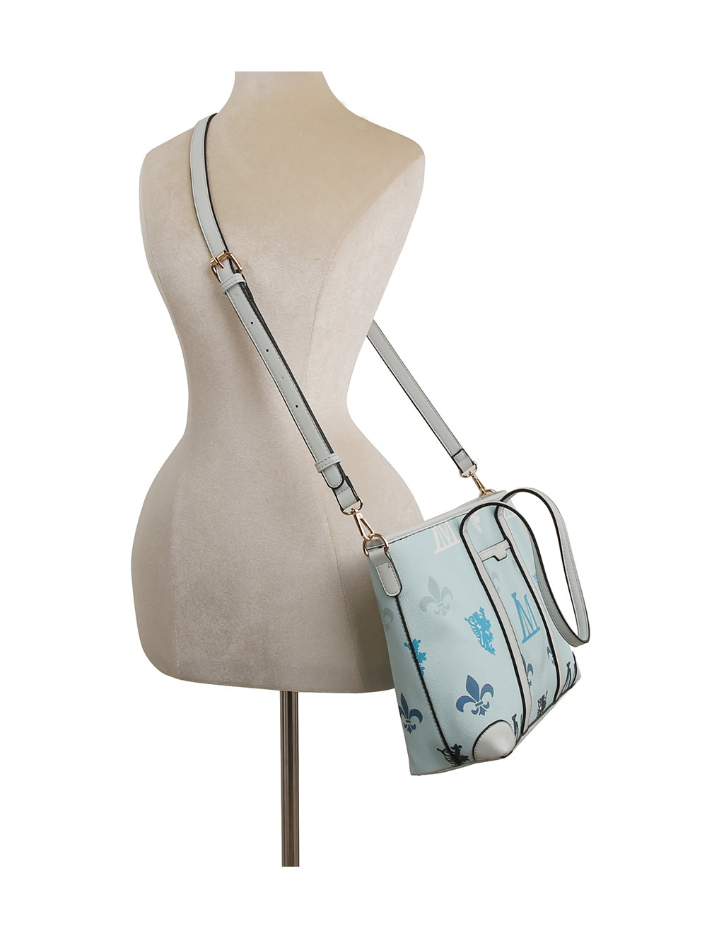 A mannequin displays the Crest Emblem Classic Tote, a light blue purse with floral and graphic prints, a long adjustable strap, gold-tone hardware, and a structured rectangular shape worn crossbody.
