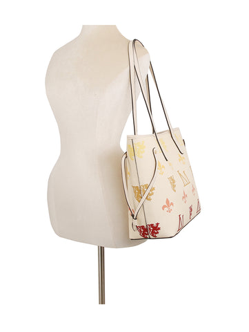 A white mannequin displays the Monogram Print Lux Faux Leather 2-Piece Tote Set in cream with multicolored symbols, black trim, two handles, structured sides, and a top zip closure against a plain white background.