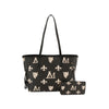 The Monogram Print Lux Faux Leather 2-Piece Tote Set features a black tote with a single strap and zip closure, plus a matching pouch. Both are adorned with white fleur-de-lis, lion head, and M logos on black faux leather, shown on a white background.