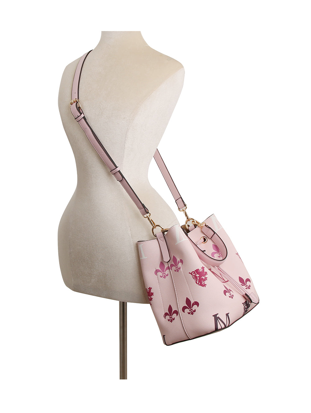 The 2 in 1 Monogram Print Faux Leather Bucket Bag features light pink faux leather with a darker pink floral and fleur-de-lis pattern, gold hardware, an adjustable shoulder strap, and a drawstring closure, shown on a dress form.
