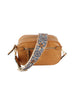 The Guitar Strap Crossbody Sling is a tan faux leather bag with gold-toned hardware and a wide, adjustable blue and white floral strap. It features two main compartments and a braided zipper pull for stylish organization.