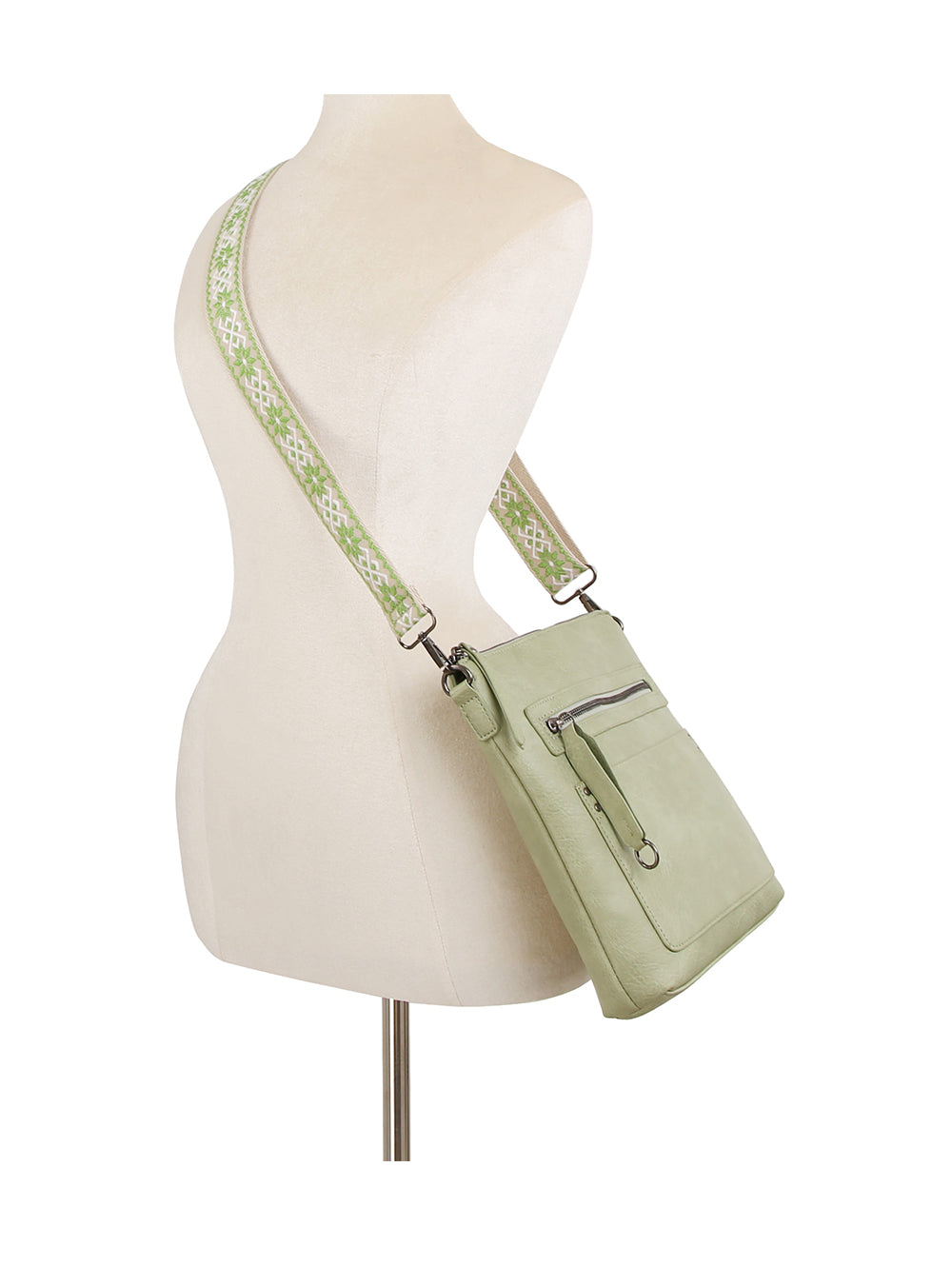 The Daily Zip Pocket Guitar Strap Crossbody Bag features light green faux leather, a front zipper pocket, a wide green and white patterned guitar strap, and silver tone hardware, shown on a dress form mannequin.