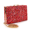 The Colorful Stone Patterned Evening Bag is a rectangular clutch with red and multicolored stones, gold edging, a gold chain strap, and luxe faux leather for an elegant look.