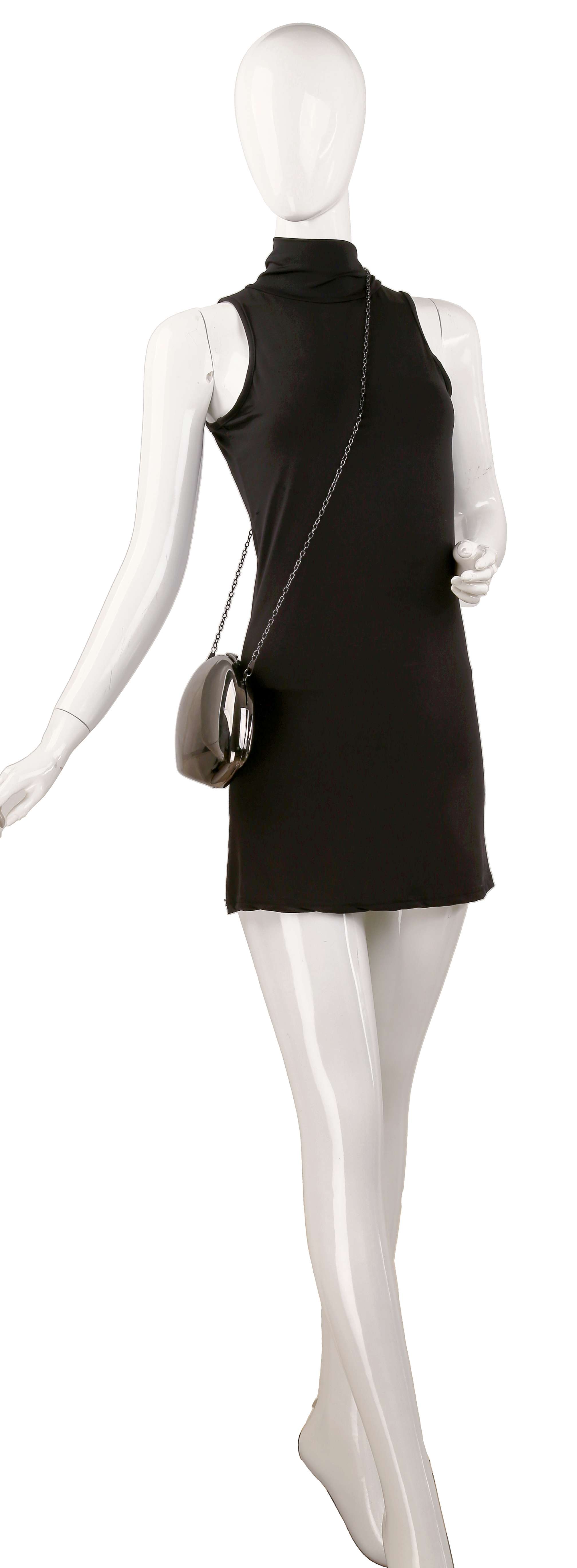 A white mannequin in a sleeveless black turtleneck mini dress poses with one arm outstretched, carrying the Modern Patent Shoulder Bag, a small and stylish modern handbag.