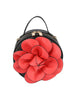 The Raised Flower Petite Handbag is a round black faux leather bag with a top handle, zip closure, and a bold red flower with black-edged petals decorates the front.