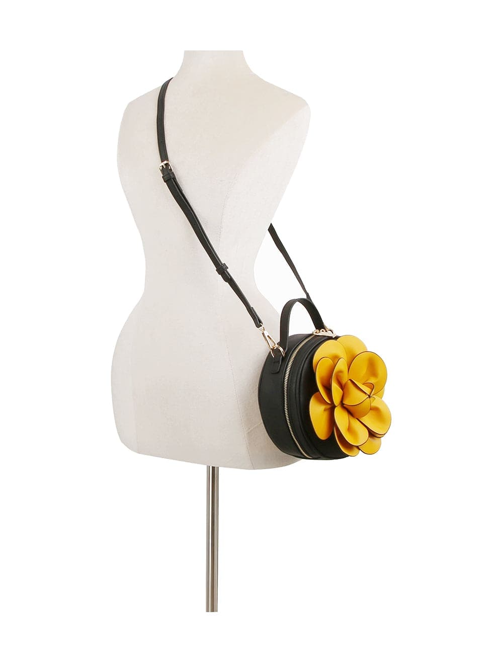 The Raised Flower Petite Handbag, a black round faux leather bag with a large yellow flower accent, is shown on a dress form. It offers a top handle, long crossbody strap, and zip closure for versatile and stylish carrying.