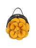 The Raised Flower Petite Handbag is a round black faux leather bag with a top handle, gold zip closure, and a large yellow raised flower with layered black-outlined petals—making it a standout accessory.